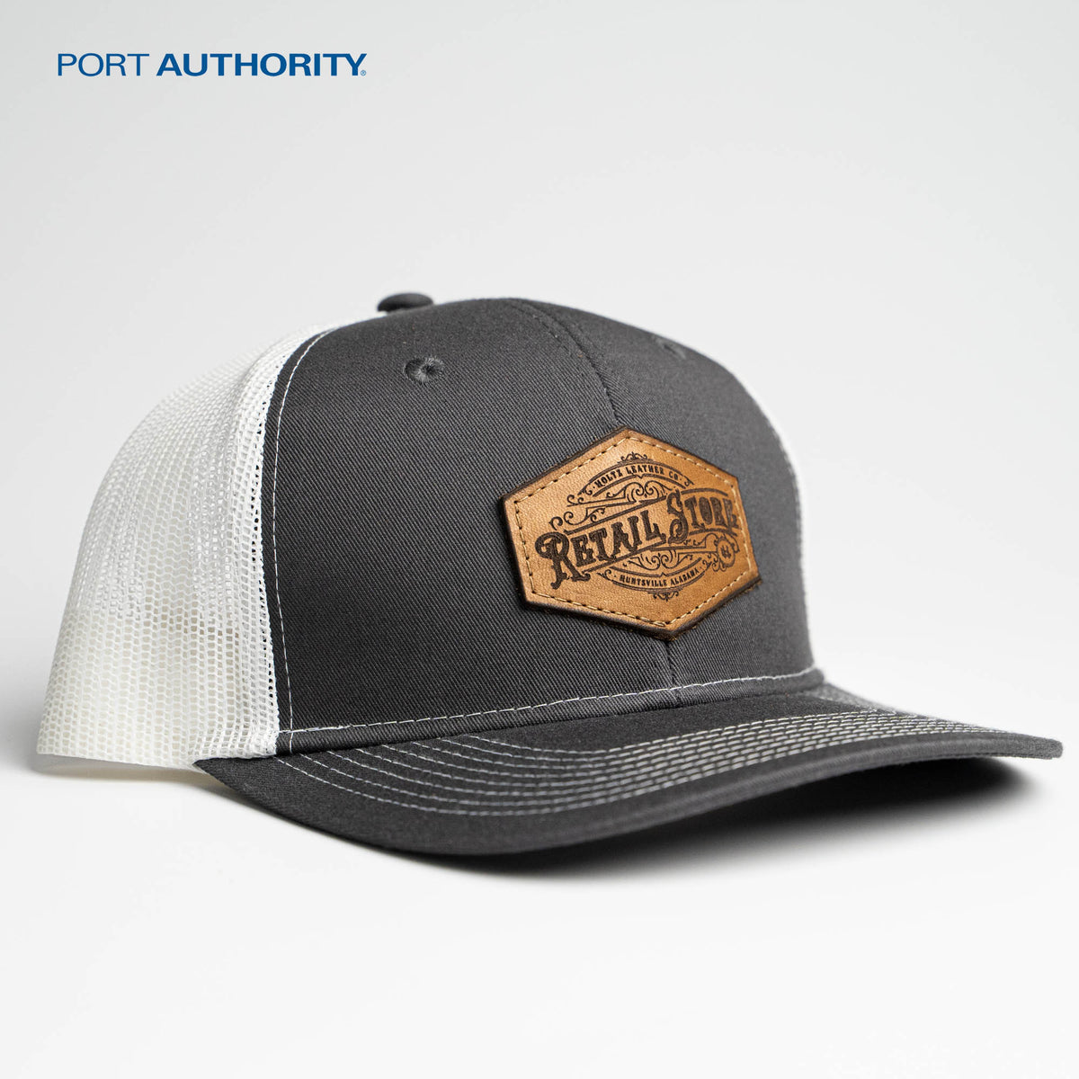 Gray and white Port Authority C112 trucker hat with custom leather patch