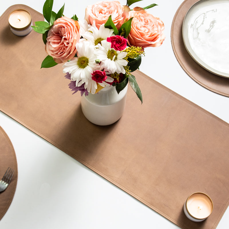 Table set with a fine leather table runner, flower, candles, and fine leather placemats